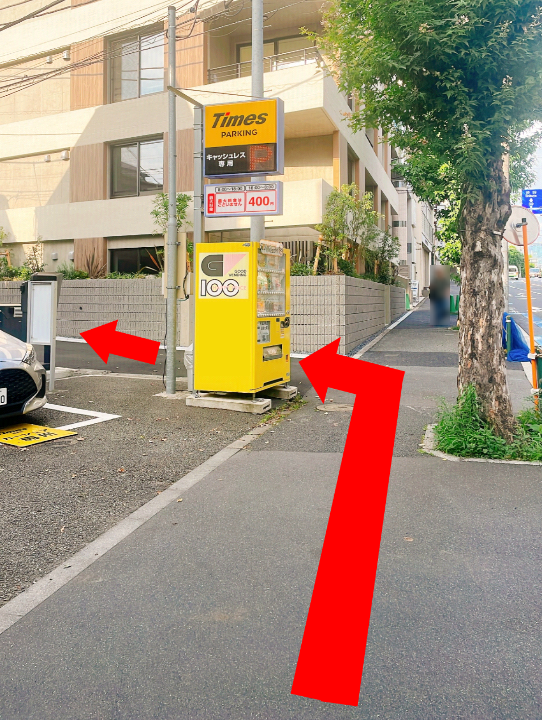 Yellow Times parking payment machine on a city sidewalk, with a tree and building behind; red arrows point left and toward the machine to indicate directions.