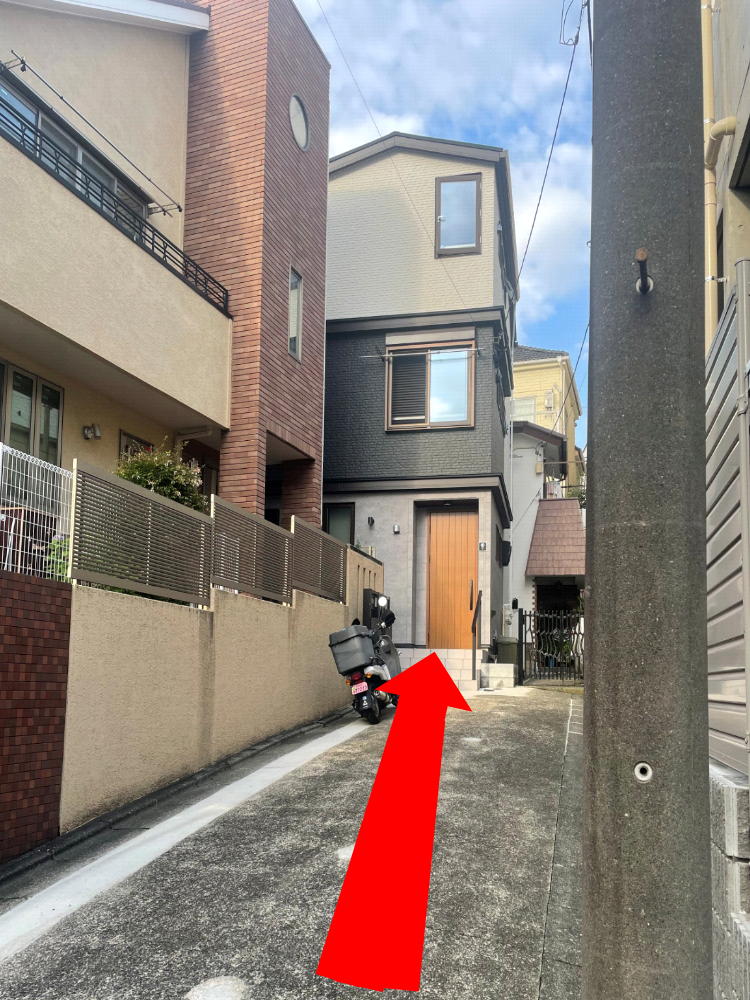 Narrow residential alley with a black scooter parked on the left and a wooden front door at the end.