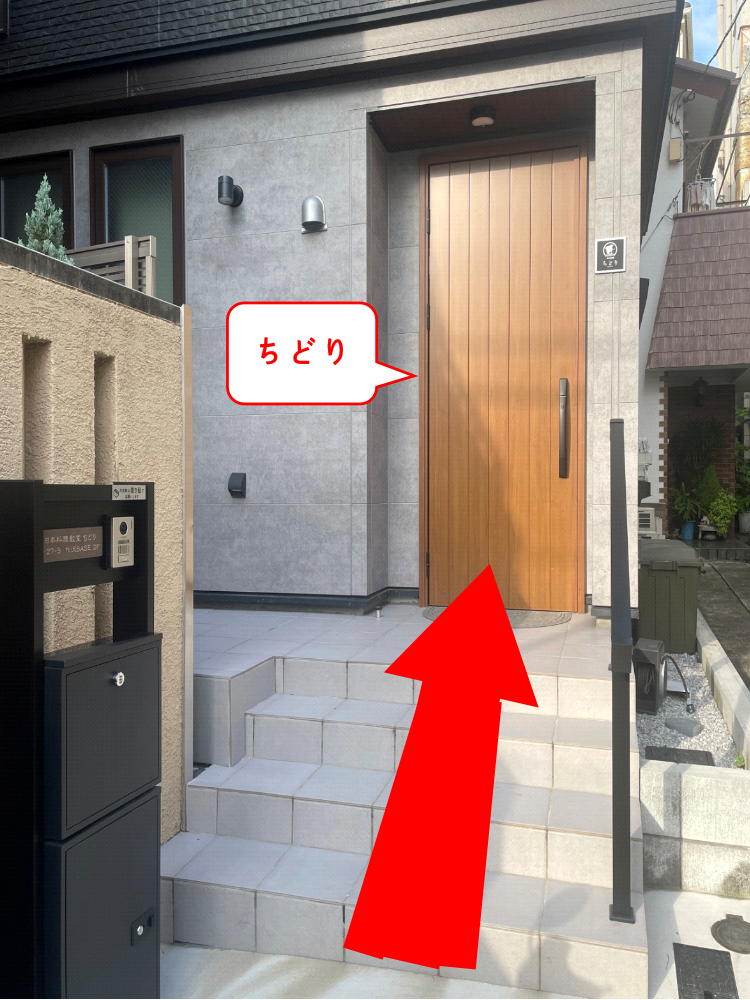 Red arrow points to a wooden front door at a modern gray-tiled entrance; speech bubble reads ちどり near the door.